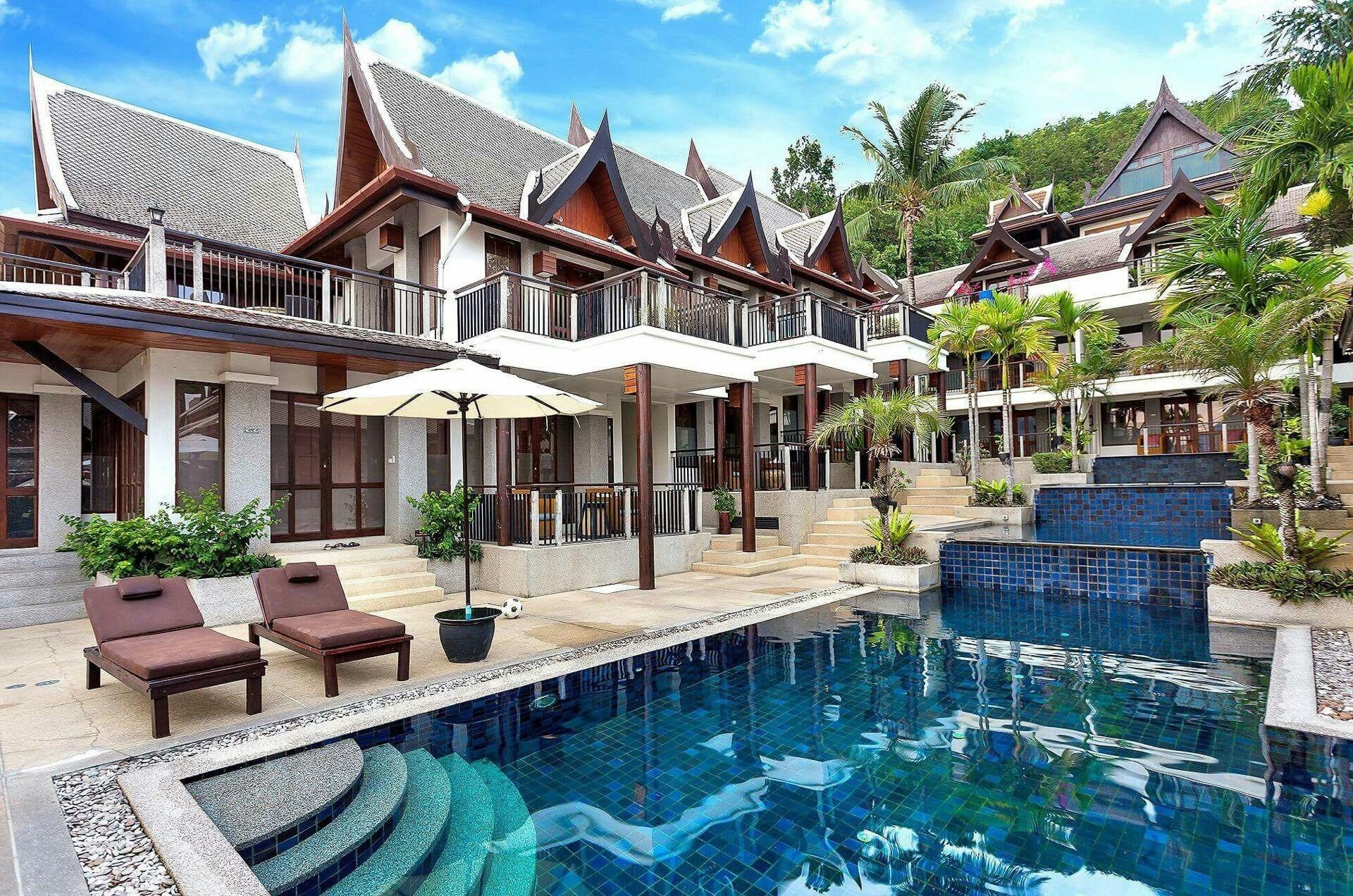 Wide pool with loungers and Thai-gable villas in daylight