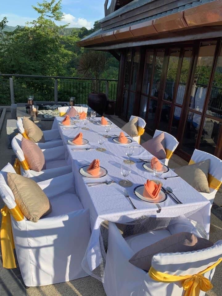 Outdoor deck dinner setup with gold sashes and orange napkins, framed by teak and the headland